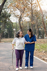 护士用助行器帮助老年妇女 护士牵着手帮助老年妇女在公园设施中行走