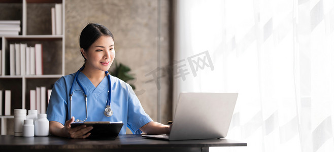 亚洲医生年轻漂亮的女人微笑着使用笔记本电脑工作，她在医院办公桌办公室的文书工作或剪贴板白皮书上写一些东西，医疗保健概念