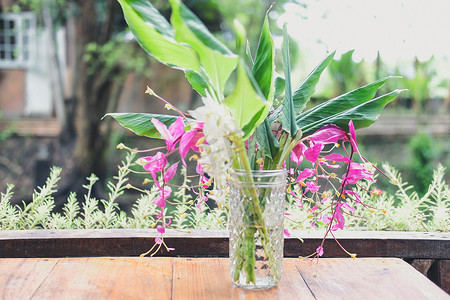 玻璃瓶装饰摄影照片_玻璃瓶中的粉红色花朵和绿叶装饰在桌子上