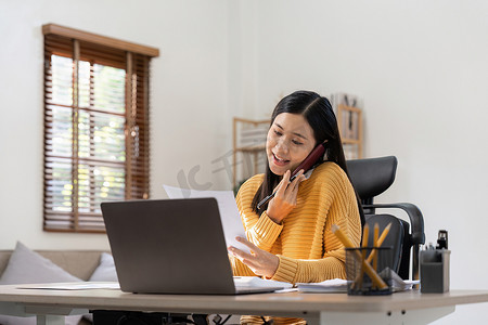 亚洲女性通过电话交谈，在办公桌上使用笔记本电脑计算器文档，计划分析财务报告、商业计划投资、财务分析概念。