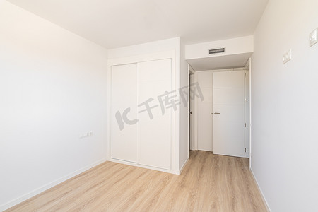 室内通风摄影照片_白色空荡荡的阳光明媚的房间，配有内置衣柜通风和两扇通往浴室和出口的门。