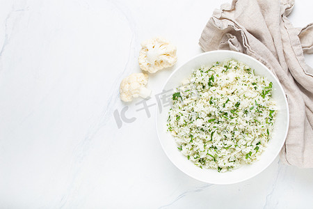 生花椰菜米或蒸粗麦粉，白碗里有莳萝，健康的低碳水化合物蔬菜配菜，用于酮饮食和健康的低热量营养，白色大理石背景，复制空间