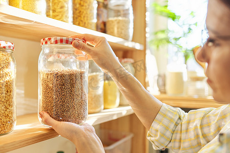 食品储藏室里的食物储存，女人手里拿着一罐荞麦