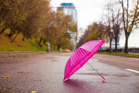 户外湿沥青上的粉色儿童伞