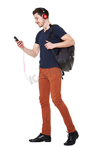 走路听音乐摄影照片_拿着手机走路，戴着耳机听音乐的年轻人