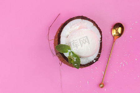白色冰淇淋球摄影照片_新鲜椰子中的香草冰淇淋球，一半用薄荷叶装饰，粉红色背景上有勺子