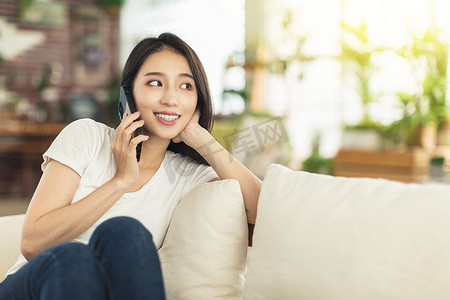 一位年轻女性坐在家里的沙发上，一边拿着手机一边聊天，悠闲而愉快地与同事讨论工作或与朋友聊天