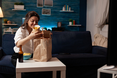 在垃圾食品送货上门时，微笑开朗的女人坐在沙发上打开快餐外卖