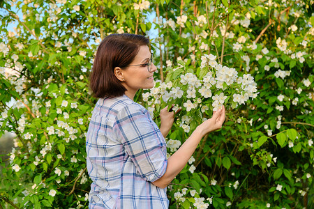 一位微笑的中年妇女的画像靠近开花的茉莉花丛。