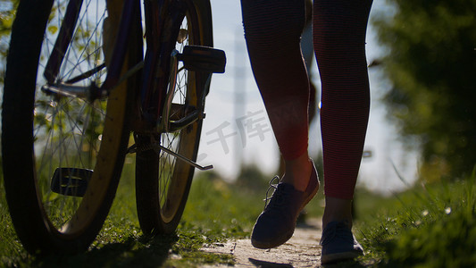 在阳光明媚的夏日，在公园的小路上骑自行车的女孩的腿，在绿色的映衬下