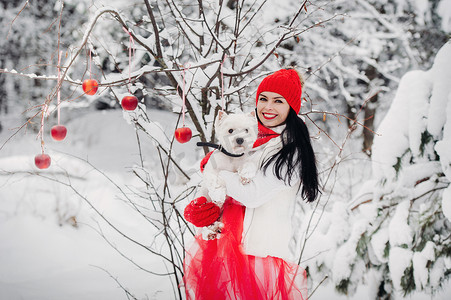一个穿着红色夹克的女人和一条狗在寒冷的冬天森林里的画像。