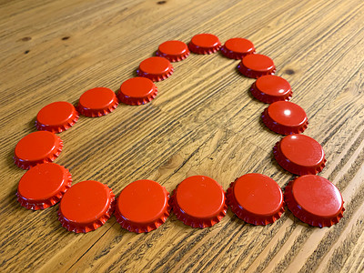 爱心饮料摄影照片_质朴的木桌上用啤酒瓶盖盖制成的红色爱心。