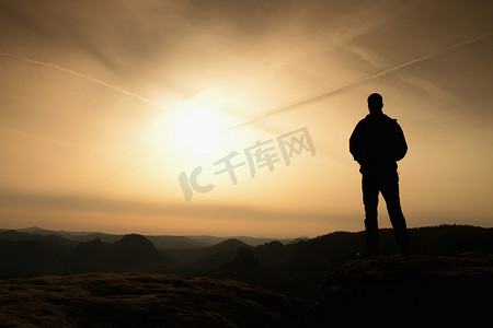 身穿黑色衣服、双手插在口袋里的运动员站在岩石帝国公园的山顶上，看着雾霭