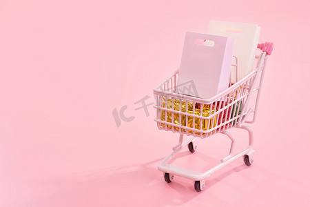 年度销售购物季概念 — 淡粉色背景中突显的装满纸袋礼品的迷你粉色购物车手推车、空白复印空间、特写