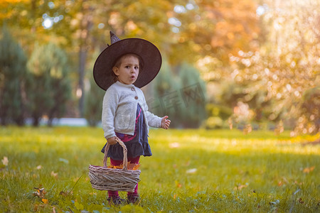 万圣节在秋天公园里穿着女巫服装的小女孩，篮子里装满了黄色的树叶。