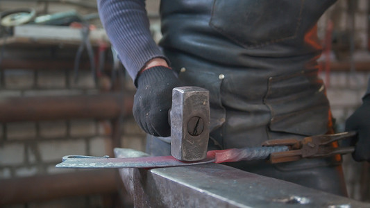 肌肉男铁匠用锤子在锻造钢刀