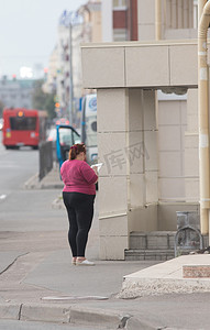 大块头的年轻女人站在镜头前，在街上的笔记本上写字