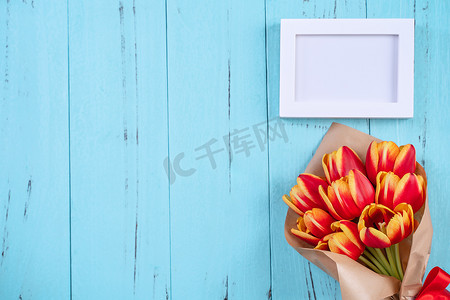 郁金香花束、相框、母亲节概念 — 美丽的红色、黄色花束、蓝色木质背景中突显的白色空白图片模板、顶视图、平躺