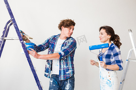 粉刷滚筒摄影照片_修理、翻新和爱情情侣概念 — 年轻的家庭一起修理和粉刷墙壁，一起笑。