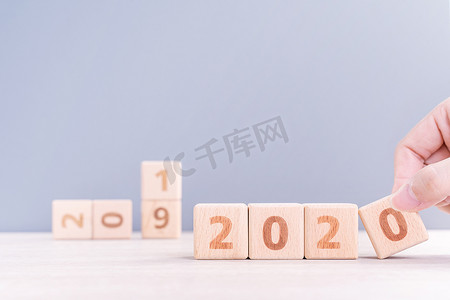 2023兔年来了摄影照片_摘要 2020 年和 2019 年新年倒计时设计理念 — 女性在木桌和蓝色背景上拿着木块立方体，特写，复制空间。