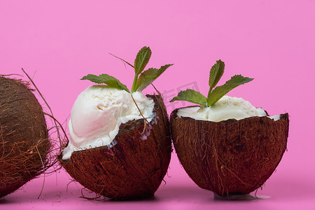 香草冰淇淋球摄影照片_粉红色背景中用薄荷叶装饰的新鲜椰子半香草冰淇淋球
