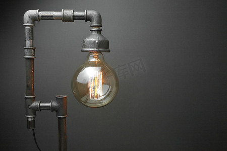 电商渐变背景摄影照片_复古灯由金属水管制成，灰色背景上有一盏爱迪生灯。