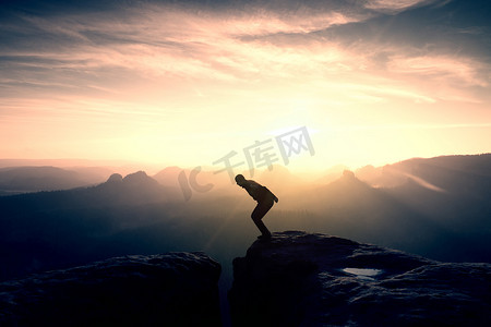 身穿黑色衣服、双手插在口袋里的运动员站在岩石帝国公园的山顶上，看着雾霭