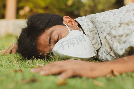 COVID19摄影照片_生病的年轻人戴着医用面罩倒在地上-概念显示生病、头晕、健康不佳、脱水或中暑。