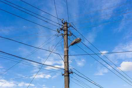 有许多电缆的混凝土灯柱在蓝天上呈放射状连接，背景为羽毛云，居中构图。