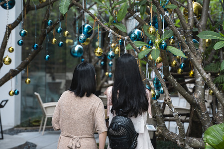 两个女孩站在装饰精美的圣诞树旁，圣诞树上摆着蓝色和金色的玩具以及漂亮的蓝色蝴蝶玩具。