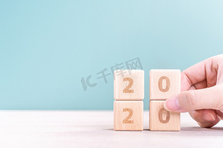 2023兔年来了摄影照片_摘要 2020 年和 2019 年新年倒计时设计理念 — 女性在木桌和绿色背景上拿着木块立方体，特写，复制空间。