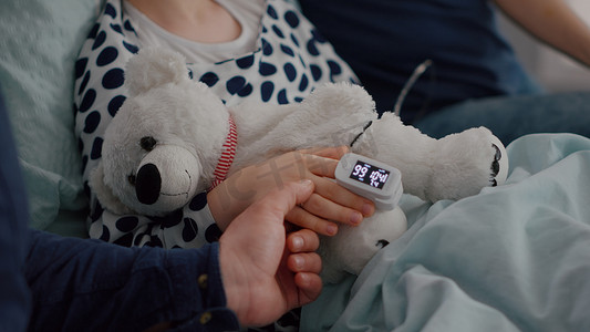 用手指上的医用血氧仪躺在床上休息的生病女儿的特写