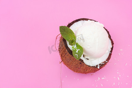 香草冰淇淋球摄影照片_新鲜椰子半块的香草冰淇淋球，装饰着粉红色背景的薄荷叶