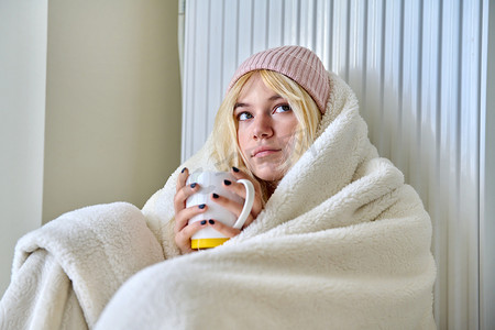 年轻的少女用毯子、暖气片、热茶取暖