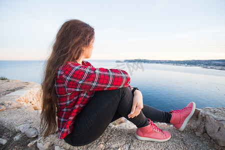 旅行、冒险和孤独的概念 — 一个女孩坐在悬崖边上望着大海