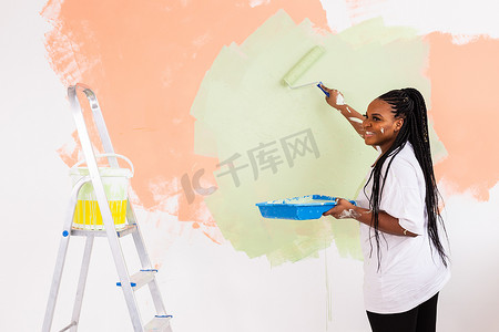 年轻快乐的非洲裔美国女人在新房子里用油漆滚筒粉刷内墙。