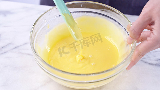 用绿色橡胶刮刀搅拌工具将蛋黄混合到蛋糕面糊中，搅拌至光滑，并在玻璃碗中充分混合，特写，生活方式
