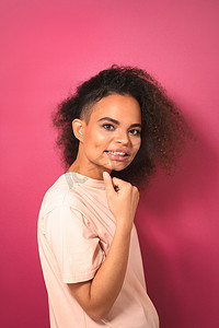 迷人热情的年轻非洲裔美国女孩，留着爆炸头，一只手臂交叉着，身穿粉红色背景中突显的桃色 T 恤，积极地看着镜头。