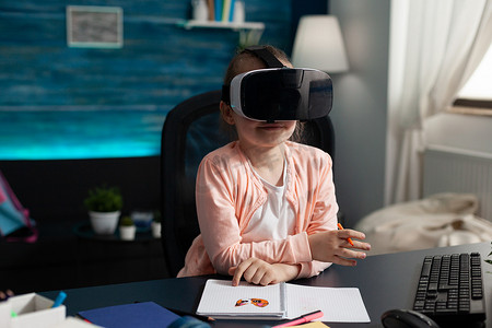 儿童数学摄影照片_坐在桌旁使用耳机体验虚拟现实的儿童