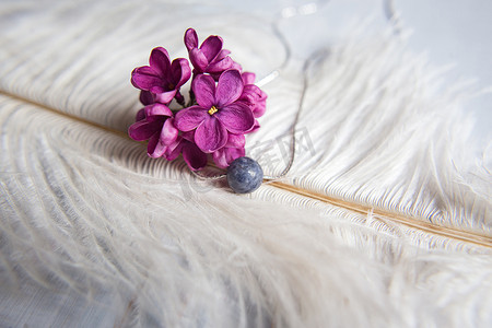 银色项链摄影照片_项链由天然石材制成，银色配件，白色鸵鸟羽毛上有紫色紫丁香花。