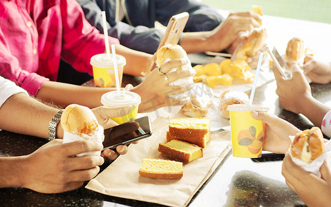 一群吃零食、忙着玩手机的人一起坐在大学餐厅 — 朋友们享受晚餐、快乐会议或吃垃圾食品并在吃饭时使用手机的概念