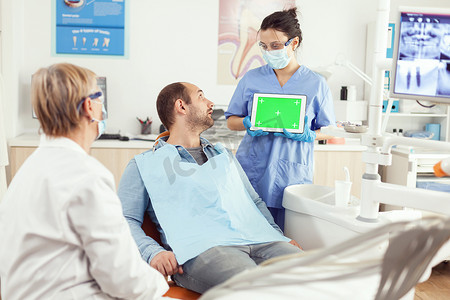 护士指着绿屏显示，而病人坐在牙科椅上