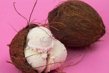 粉红色背景中用薄荷叶装饰的空椰子中的香草冰淇淋球