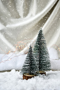 雪花圣诞树摄影照片_香槟色丝绸背景和白雪上的两棵圣诞树。