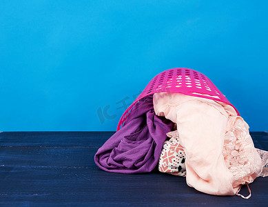 浴室衣服摄影照片_蓝色背景上装满衣服和亚麻布的粉色塑料篮