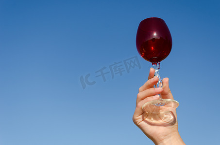 手握蓝天上的红葡萄酒杯蠕动茎