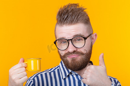 一个有趣、自信、英俊的年轻人的肖像，戴着眼镜，留着胡子，黄色背景上有一个黄色小杯子。