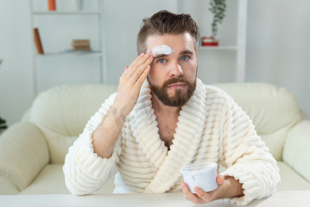 留胡子的家伙在镜子前涂抹面霜 皮肤护理和水疗中心的男士概念。