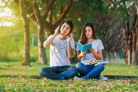 年轻夫妇在公园里用耳机看书和听音乐