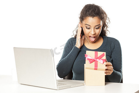 礼物盒子打开摄影照片_办公桌前拿着笔记本电脑的非洲女人打开了一个装有礼物的盒子